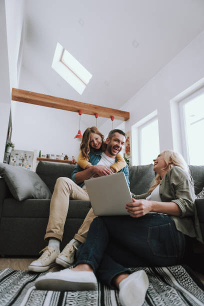 happy family watching videos on laptop and laughing - couple home interior laptop computer imagens e fotografias de stock