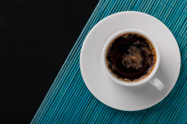 istock Top view of a black coffee cup on blue bamboo mat and black textured background. 1132988728
