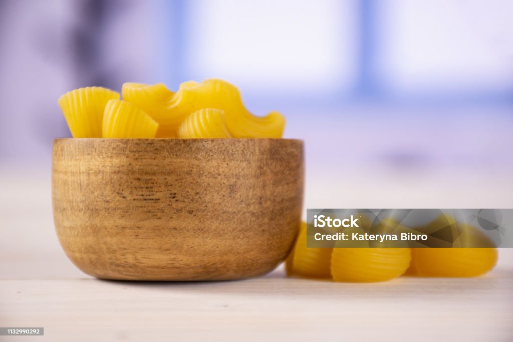 Raw pasta pipe rigate with blue window Lot of whole yellow raw pasta pipe rigate variety with wooden bowl with blue window Blue Stock Photo