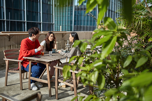 Male and female friends sitting at cafe table. Man and women are talking on terrace. They are spending leisure time in cafeteria.