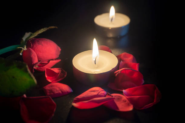 Two tea candles, red rose petals with shallow depth of focus with reflection on black background