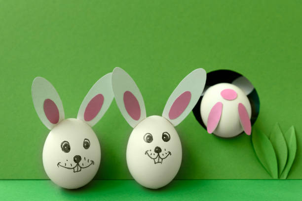 卵と紙の耳から作られたイースターバニーは、緑のパステル背景に穴にジャンプします。創造的なアイデア。アートフードのコンセプト。 - bunny painting ストックフォトと画像