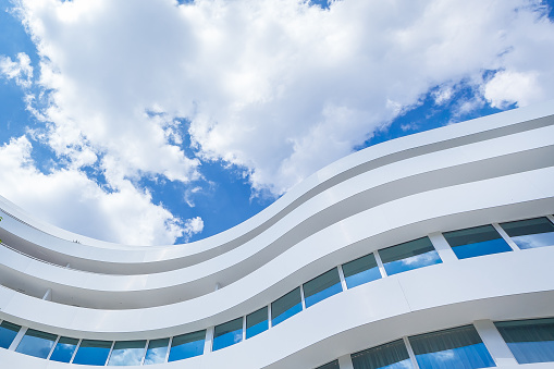 Exterior Of Curved Glass Modern Office Building on a Blue Cloudy Sky Background.