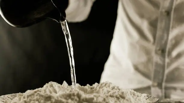 Photo of The cook pours water on the flour from the jug in the kitchen