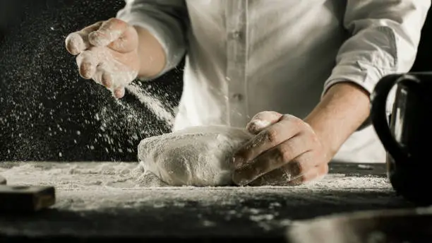 Male chef hands knead dough with flour on kitchen table side view