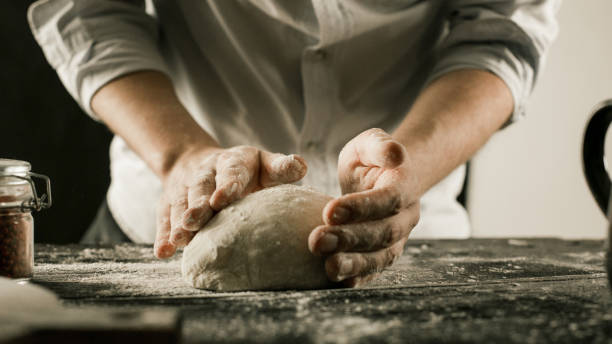 Male chef hands knead dough with flour on kitchen table