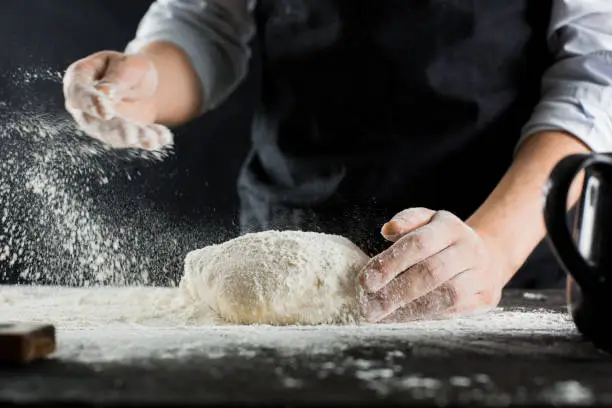 A chef in a black apron sprinkles flour on the kitchen table with flour side view