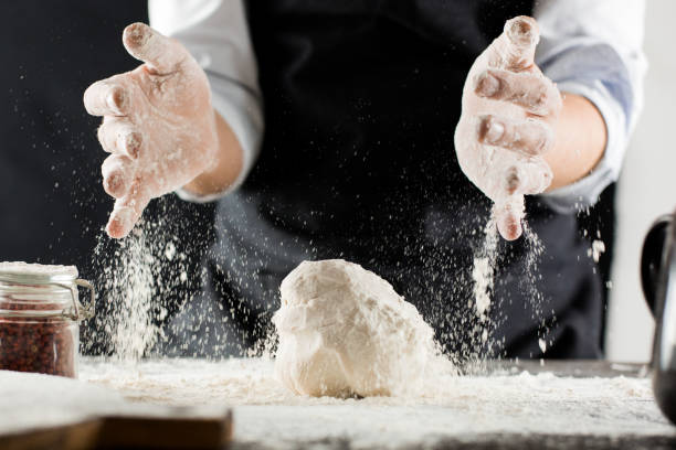 cook kneads dough with flour on kitchen table - cake making mixing eggs imagens e fotografias de stock