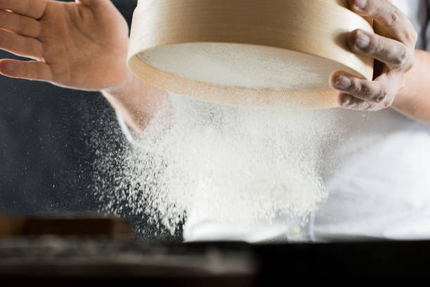 male hands of a cook sifting flour through a sieve in the kitchen - cake making mixing eggs imagens e fotografias de stock