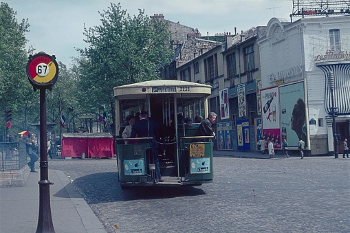 Paris, Il de France, France, 1962. A bus departs from a stop on a Parisian street. A controller in the back of the bus sells tickets to the passengers. Furthermore: houses, billboards and pedestrians.