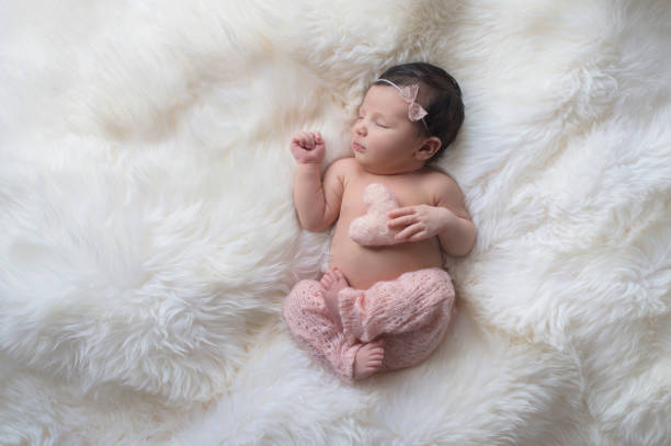 Sleeping Newborn Baby Girl with Heart Shaped Pillow Sleeping, week old newborn baby girl wearing light pink, knitted pants and holding a tiny, heart shaped pillow. Shot in the studio on a white sheepskin rug. babies only photos stock pictures, royalty-free photos & images