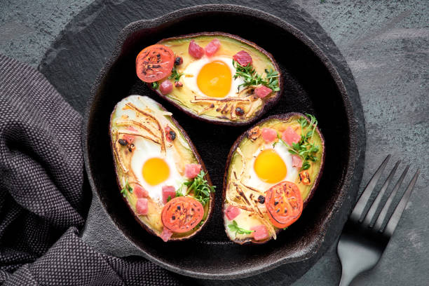 istock Keto diet dish: avocado boats with ham cubes, quail eggs, cheese and cherry tomatoes on iron cast skillet 1133004803