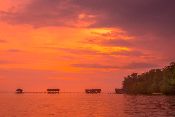 Indonesia. Raja Ampat archipelago. Coast of the island with a pier for boats. Calm ocean and orange sunset.