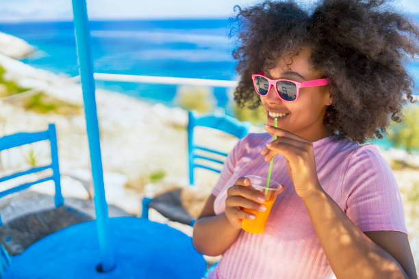 afro kobieta korzystających letnie wakacje i picie soku - summer beach multi colored vacations zdjęcia i obrazy z banku zdjęć