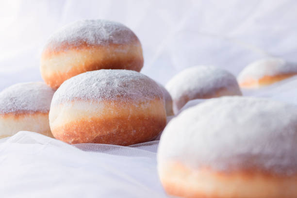 Jelly filled doughnuts with powdered sugar on a bed with white sheets