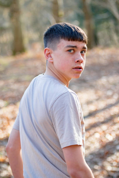 Scared or nervous teenage caucasian boy walking away through woodland on a warm spring day looking over his shoulder