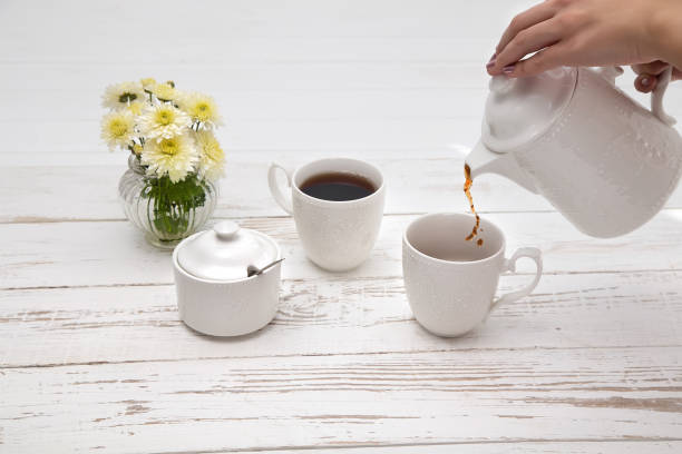 istock hands pours tea in cup of tea on wooden white table 1133019596