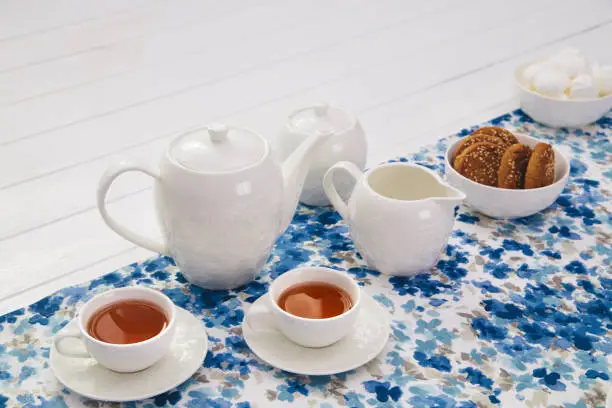 cups of tea with milk, cream and biscuits on wooden white table background with copyspace