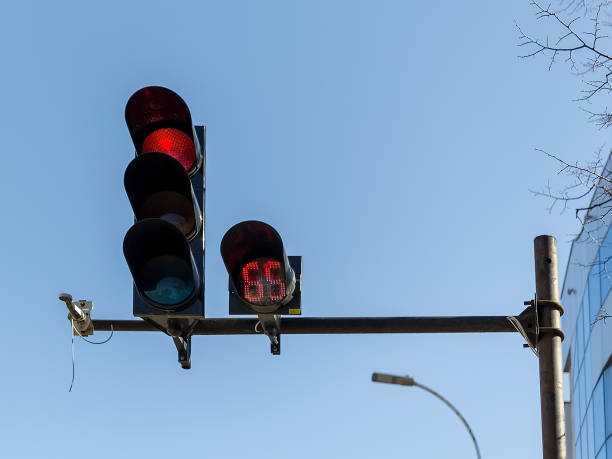istock Red car traffic light and countdown timer installed on a pole above a roadway on a city street against a blue sky. 1133022343