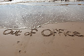 Out of Office written in the sand on a beach.