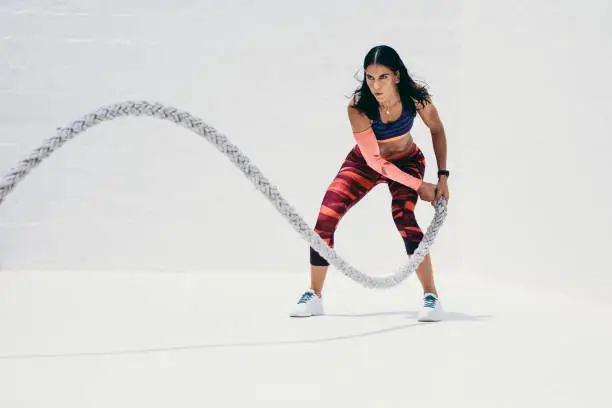 Fitness woman doing strength training using battle rope. Athletic woman doing workout with battle rope.
