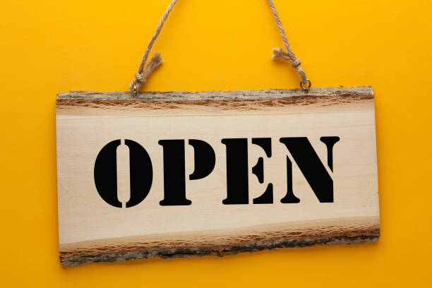 Open word on wooden sign hanging on a rope on yellow background.