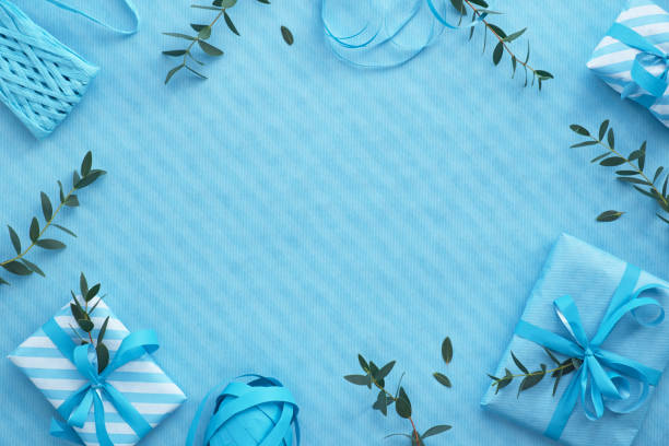 istock Blue background with wrapped gift boxes and eucalyptus twigs around empty wooden frame 1133031766