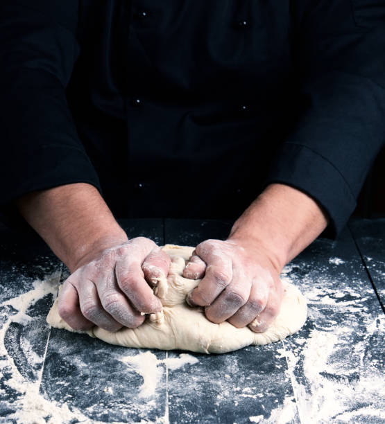 chef in black uniform kneads white wheat flour dough