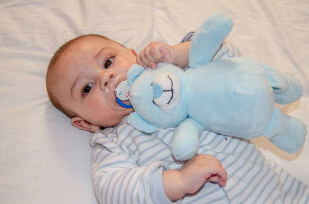 Baby accessories concept. Top view photo of knitted teddy-bear toy tiny booties and pacifier on isolated pastel blue background with copyspace