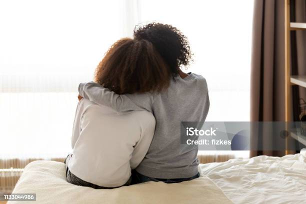 Rear View African Mother And Daughter Embracing Sitting On Bed Stock Photo - Download Image Now