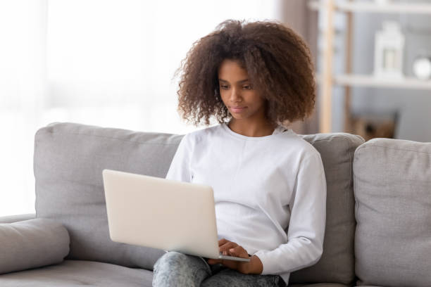 chica adolescente africana sentada en el sofá usando la computadora - african descent addiction african ethnicity rudeness fotografías e imágenes de stock
