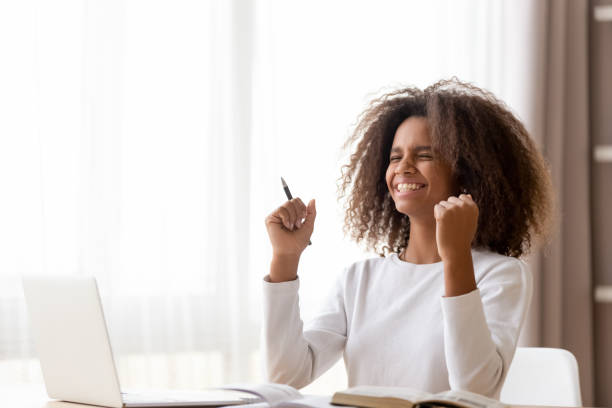 colegiala africana sentada en el escritorio se siente feliz recibido gran noticia - setting goals fotografías e imágenes de stock