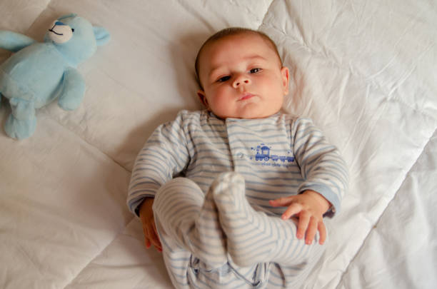 istock cute 4 months old baby boy lying on bed and playing with his legs 1133045077