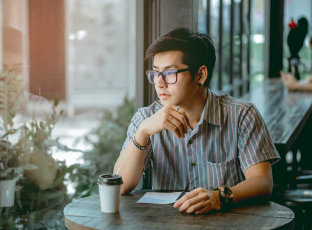 istock Asian guy with glasses sitting and writing something with thought. 1133053284