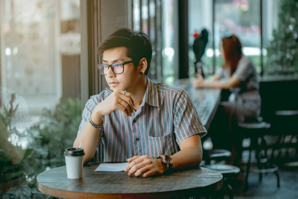 istock Asian guy with glasses sitting and writing something with thought. 1133053435