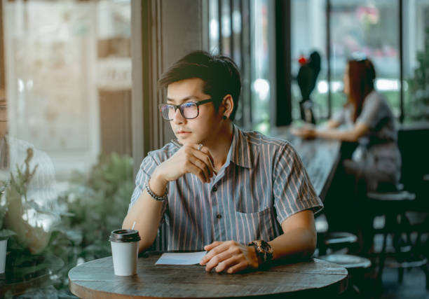 istock Asian guy with glasses sitting and writing something with thought. 1133053476