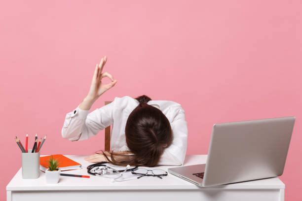 istock Female doctor laid her head down on desk, work on computer, medical document in hospital isolated on pastel pink wall background. Woman in medical gown stethoscope show ok. Healthcare medicine concept 1133055809