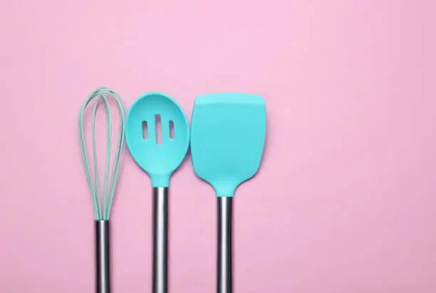 Set of tools for cooking on pink background. Silicone paddles with metal handles, whisk. Top view. Copy space.