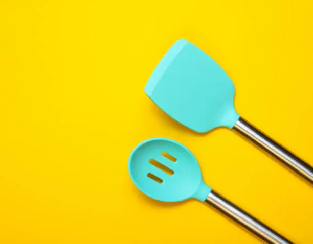 Set of tools for cooking on yellow background. Silicone paddles with metal handles. Top view. Copy space.