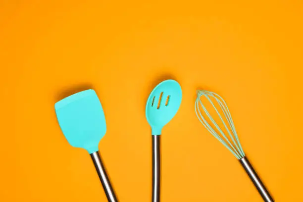 Set of tools for cooking on yellow background. Silicone paddles with metal handles, whisk. Top view. Copy space