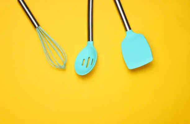 Set of tools for cooking on yellow background. Silicone paddles with metal handles, whisk. Top view. Copy space.