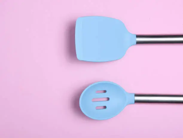 Set of tools for cooking on pink background. Silicone paddles with metal handles. Top view. Copy space.