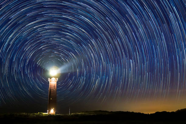 faro nocturno con senderos de estrellas en el centro - star trail galaxy pattern star fotografías e imágenes de stock