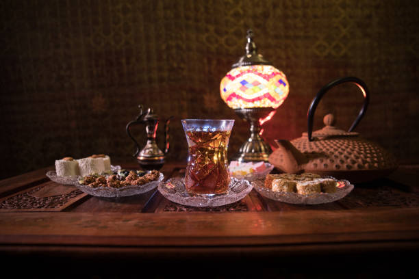 istock Arabian tea in glass with eastern snacks on vintage wooden surface. Eastern tea concept. Low light lounge interior with carpet. Empty space. 1133059864