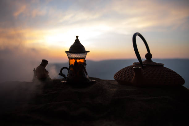 istock Arabic tea in traditional glass and pot on desert at sunset. Eastern tea concept. Artwork decoration on sand with tea. 1133059900