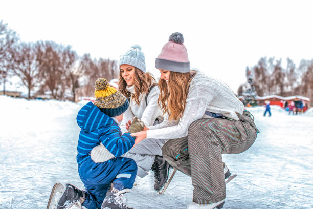 eine junge mutter mit einer freundin hebt einen kleinen jungen sohn 4-5 jahre. eislaufen im winter im park. fröhlich lächelnd, auf dem eis reiten, die art einer jungen familie, pflege und unterstützung. - 4 5 years flash stock-fotos und bilder