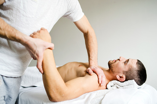 Fisioterapeuta masculino dando masaje deportivo al joven hombre en el salón photo