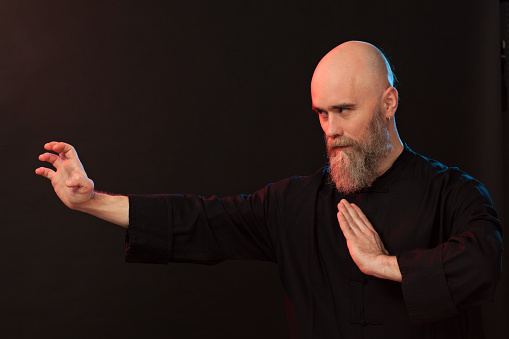 Studio portrait of a 40 year old bearded man in a black kimono doing kung fu on a black background