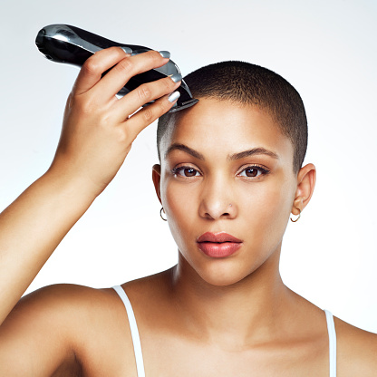 Studio shot of a beautiful young woman shaving her head against a white background