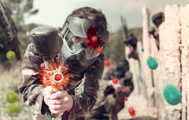 Portrait of young woman in full gear playing paintball on open b Portrait of young cheerful woman in full gear playing paintball on open battlefield paintball photography stock pictures, royalty-free photos & images